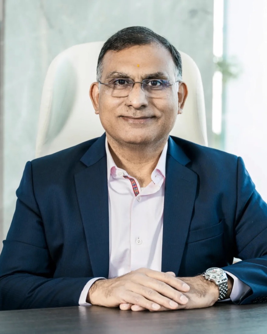Dhiren Vora, seated at his desk in a navy blazer, smiling at the camera